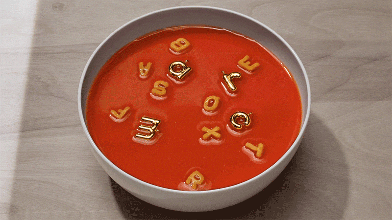Overhead view of alphabet soup featuring golden letter-shaped pasta noodles floating in a bowl of bright red tomato soup.