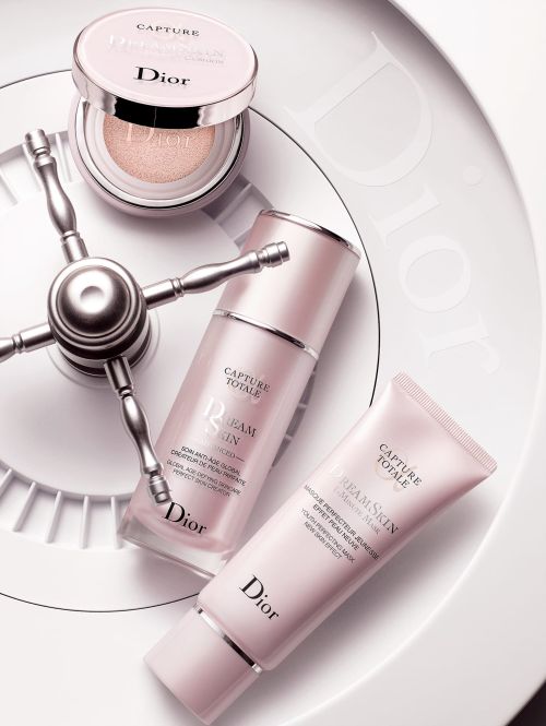 Still life showcasing Dior Capture Totale skincare products, including a foundation compact, cream, and mask, on a white surface.