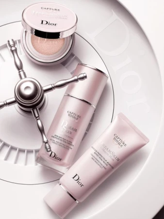 Still life showcasing Dior Capture Totale skincare products, including a foundation compact, cream, and mask, on a white surface.