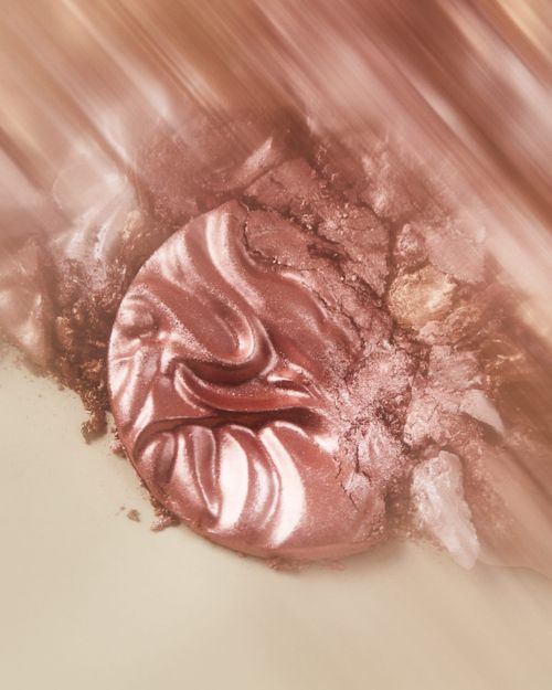 Macro photograph of a shimmering, swirling pattern of cosmetic makeup in shades of rose gold, peach, and brown for beauty concept.