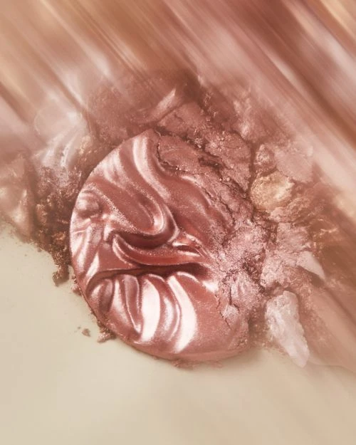 Macro photograph of a shimmering, swirling pattern of cosmetic makeup in shades of rose gold, peach, and brown for beauty concept.