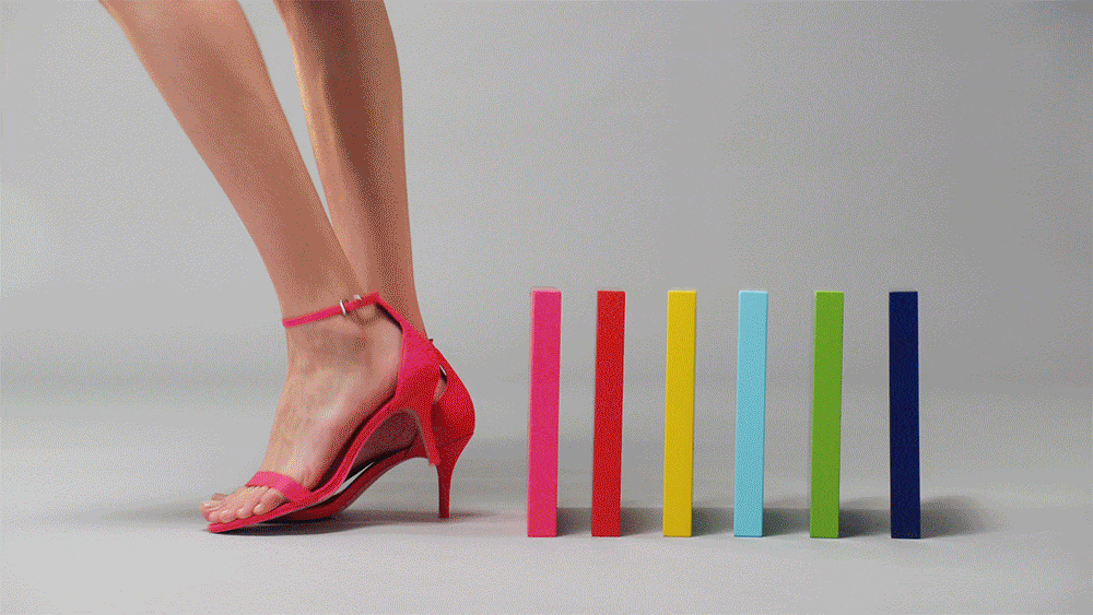 Leg of a woman in a pink high heel sandal about to step on colorful rectangular blocks, studio shot on gray background.