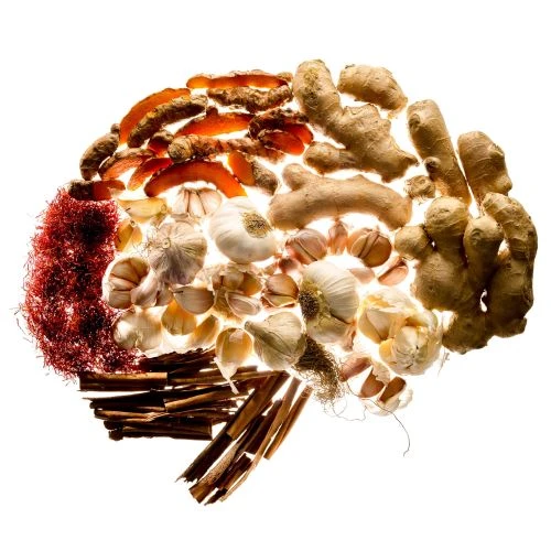 Overhead shot of a brain-shaped composition of turmeric, ginger, garlic, saffron, and cinnamon sticks, arranged on a white background.