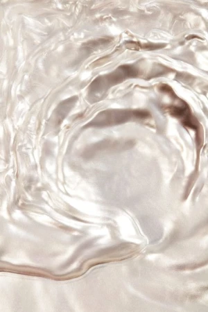 Close-up abstract texture featuring rippled waves of shimmering, reflective white and silver material, creating a fluid, pearlescent background.