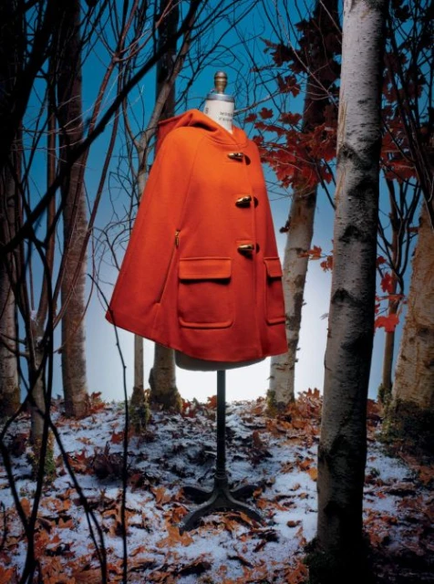 Red hooded cape coat on a mannequin in an outdoor snowy forest setting, fashion photography, studio shot.