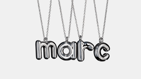 Four silver letter necklaces spelling marc hanging against a plain white background with polished metal reflections.