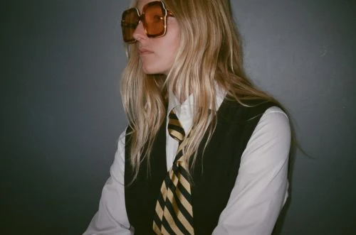 Model wearing oversized tinted sunglasses, white shirt, dark vest, and striped tie in New York fashion styling by Calvy Click.