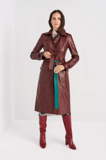 A stylish adult woman poses in a studio wearing a red leather coat, a patterned dress, and matching heeled boots against a clean white backdrop.