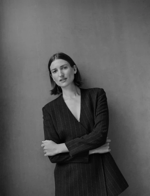 Black and white portrait of an adult female with short brown hair wearing a pinstripe jacket in front of a solid wall.