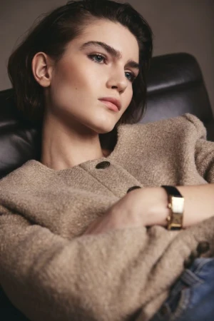 Portrait of a brunette adult female in a beige wool jacket and jeans, seated indoors, with soft lighting and a shallow depth of field.