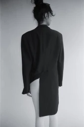 Model seen from behind wearing an oversized black blazer with tails against a plain studio background.