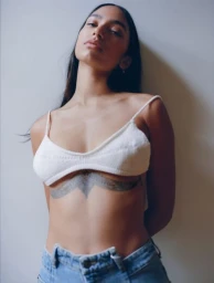 Woman wearing a white bralette and blue denim jeans posing against a plain wall in New York