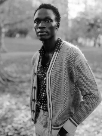 Black man wearing a patterned cardigan and polka dot shirt standing outdoors styled by Calvy Click in New York