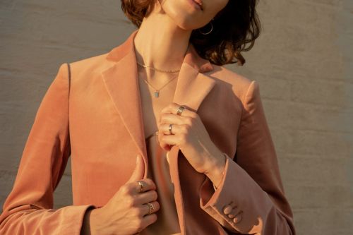 Close-up of a woman wearing a peach-colored velvet blazer and jewelry against a neutral backdrop, bathed in soft, warm light.