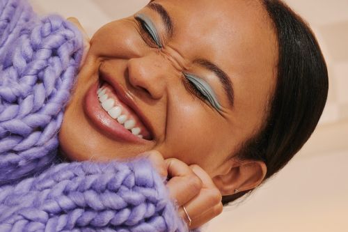 Close-up portrait of a smiling woman wearing a chunky purple knit sweater with light blue eyeshadow in New York.