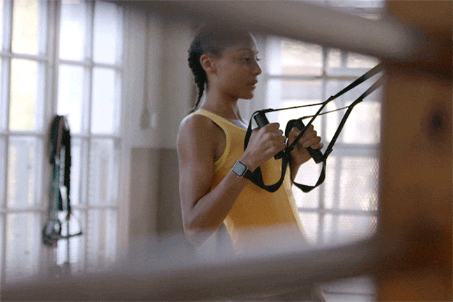 Athletic Black woman in yellow tank top does TRX suspension training in a bright studio. Modern workout gear and active lifestyle. 