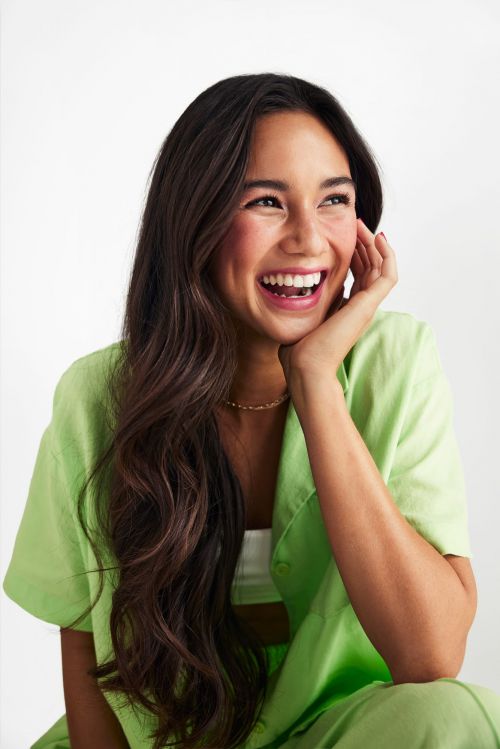 Portrait of a smiling woman with long brown hair wearing a green outfit in a bright studio. Beauty, fashion, and lifestyle concept.