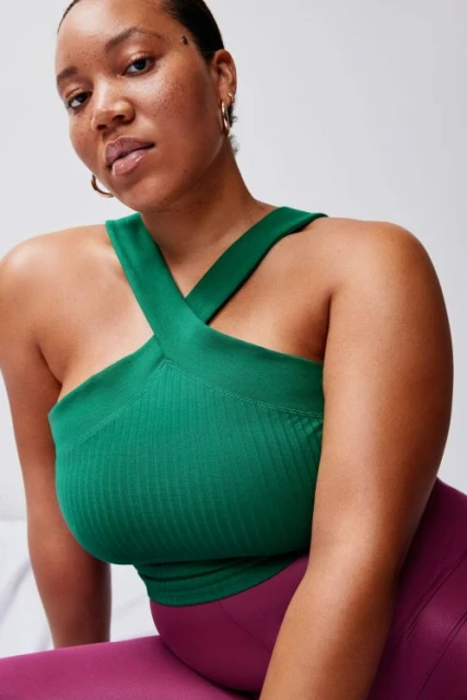 Woman wearing a green cross-front ribbed tank top and magenta leggings, posing in front of a white wall.