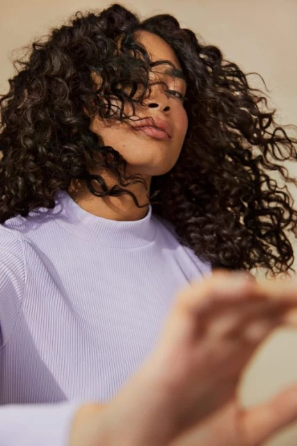Portrait of a woman with curly hair wearing a lilac long-sleeve shirt. Beauty and fashion portrait shot in a photo studio.