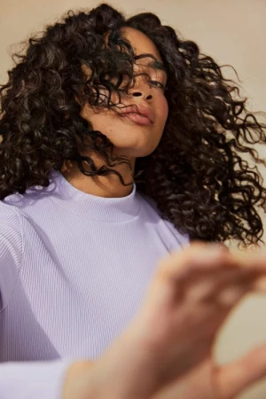 Portrait of a woman with curly hair wearing a lilac long-sleeve shirt. Beauty and fashion portrait shot in a photo studio.