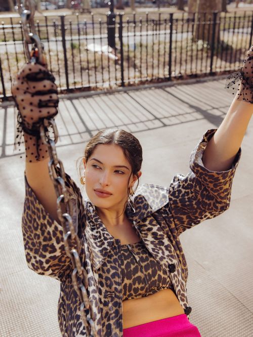 Woman wearing leopard print jacket and fuchsia skirt on a swing in an outdoor park setting on a sunny day.