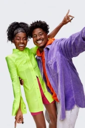 Black woman in neon green shirt and black man in purple jacket posing together against a plain white background