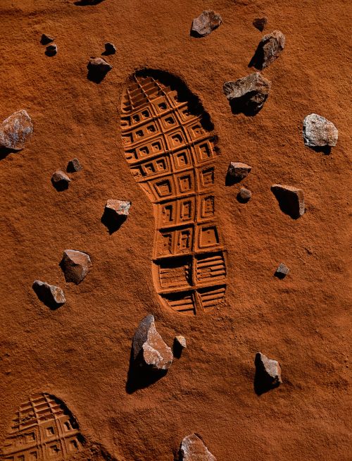 Footprint in red sand with scattered rocks creates an otherworldly scene reminiscent of a martian surface, emphasizing exploration and solitude.