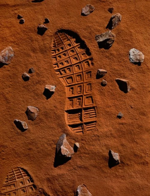 Footprint in red sand with scattered rocks creates an otherworldly scene reminiscent of a martian surface, emphasizing exploration and solitude.