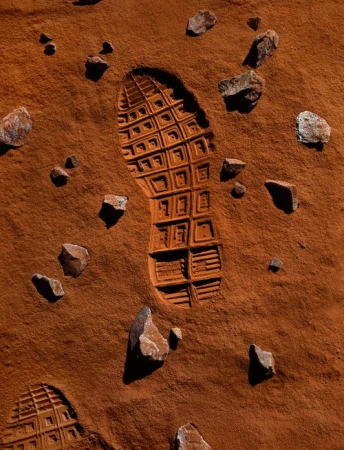 Footprint in red sand with scattered rocks creates an otherworldly scene reminiscent of a martian surface, emphasizing exploration and solitude.