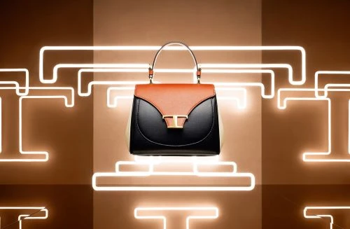 Fashionable black and tan satchel handbag with a gold clasp, presented on a warm brown backdrop with glowing geometric shapes.