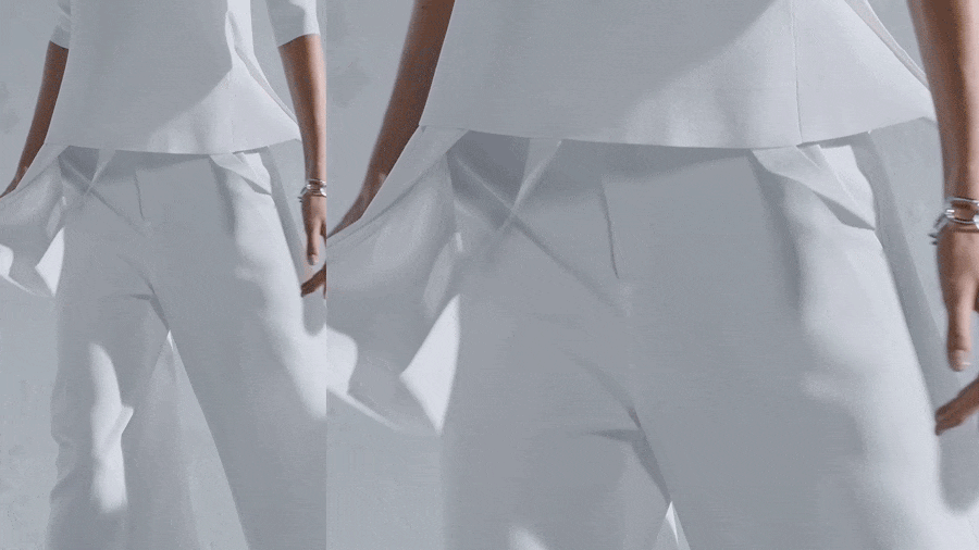 Close-up of a model wearing a white top and trousers with draped layers against a neutral background.