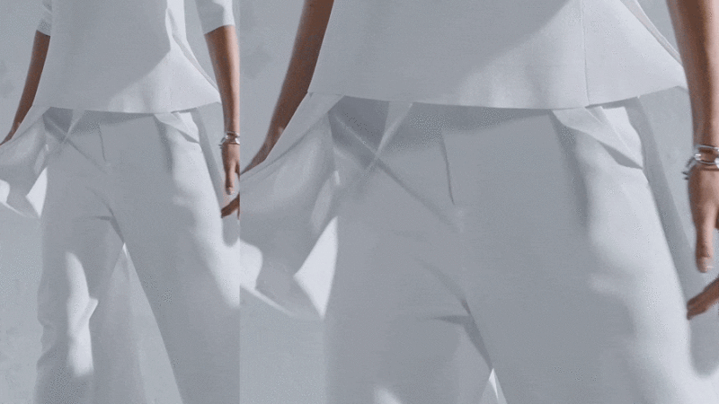 Close-up of a model wearing a white top and trousers with draped layers against a neutral background.