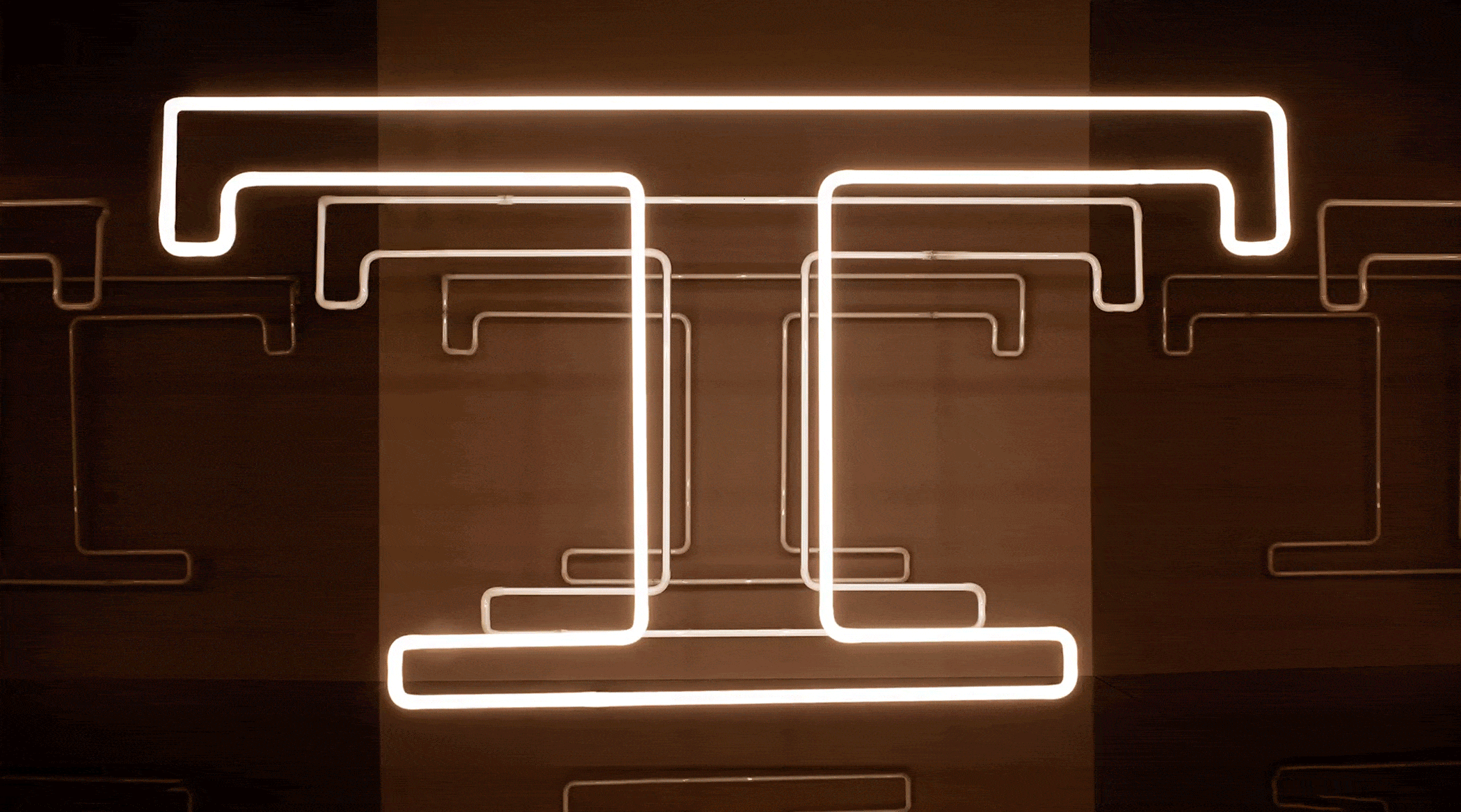 Abstract neon light art installation with geometric shapes on a dark brown background creates a modern, glowing design.