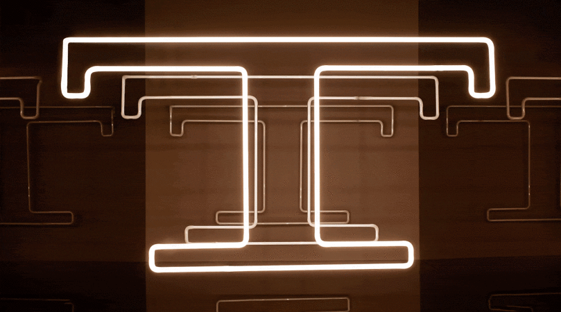 Abstract neon light art installation with geometric shapes on a dark brown background creates a modern, glowing design.