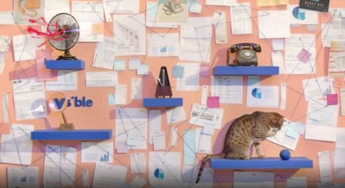 Interior scene features a cat playing on a shelf, surrounded by office items such as a fan, metronome, telephone, and papers.