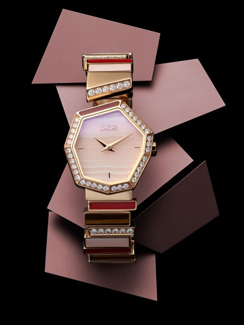 Close-up of an elegant women's Dior watch with a silver, gold, and jewel-encrusted bracelet on a black surface with purple geometric shapes.