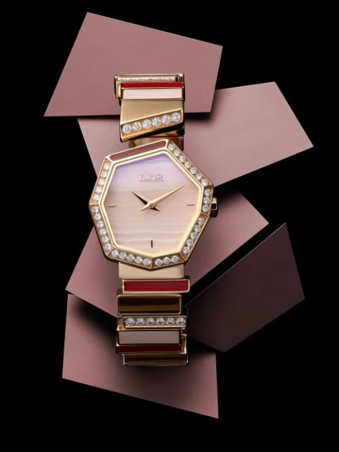 Close-up of an elegant women's Dior watch with a silver, gold, and jewel-encrusted bracelet on a black surface with purple geometric shapes.