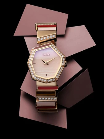 Close-up of an elegant women's Dior watch with a silver, gold, and jewel-encrusted bracelet on a black surface with purple geometric shapes.