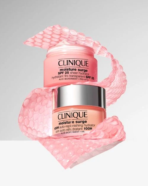Two pink Clinique Moisture Surge moisturizer jars are stacked on each other surrounded by a pink textured material. Beauty product shot.