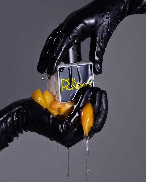 Perfume bottle held by two hands in black latex gloves, with peach slices and dripping liquid on a grey background, studio shot.