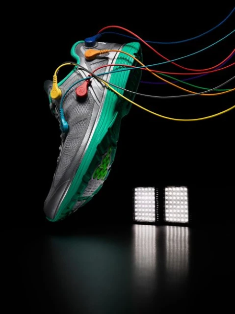 Studio shot of a gray and green running shoe adorned with colored wires and electrical connectors, against a black backdrop with LED lighting.