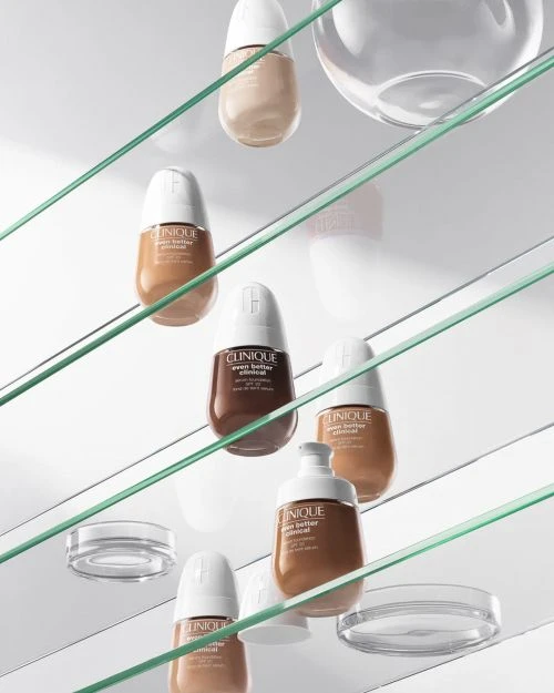 Multiple bottles of Clinique Even Better Clinical foundation are displayed on glass shelves with a light and airy background.