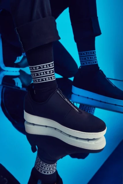 Close-up of two black and white platform sneakers with text-patterned socks on a reflective blue surface, showcasing fashion footwear.