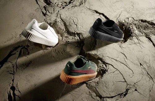 Three Puma platform sneakers are featured in black, white and dark green with dark red stripe, set against a cracked grey surface.
