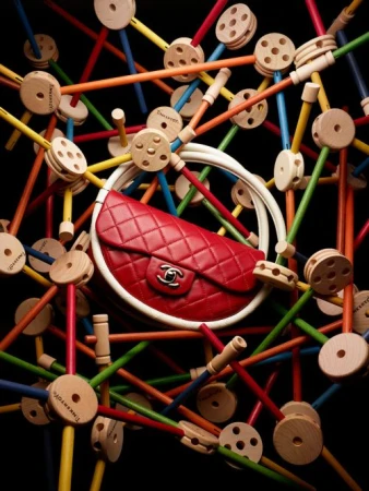 Red Chanel handbag with white trim surrounded by colorful wooden Tinkertoy construction pieces on a black background in a studio shot.