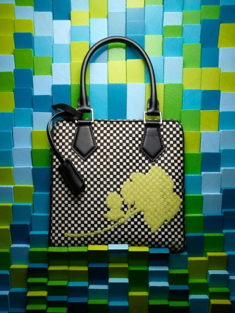 Checkered handbag with black handle and lime green floral design on a multi-colored blue and green wooden block background.