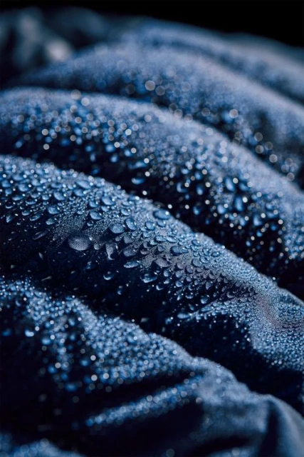 Close-up shot of a water-resistant, navy blue puffer jacket with tiny water droplets beading on the surface, creating a textured effect.