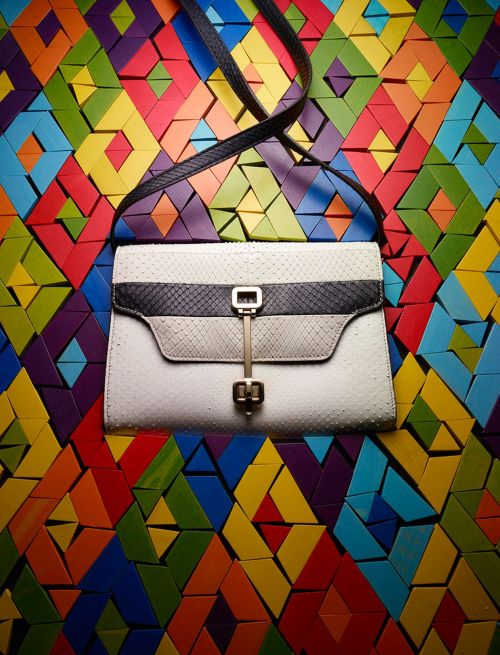 Stylish white clutch purse with black snakeskin trim, hanging against a colorful geometric background. Fashion accessory photography.