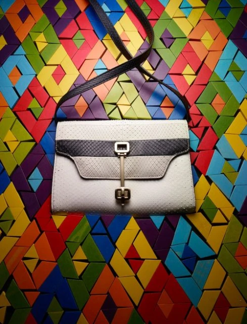 Stylish white clutch purse with black snakeskin trim, hanging against a colorful geometric background. Fashion accessory photography.