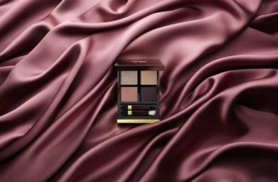 An eyeshadow quad palette rests centrally on a smooth, draped mauve satin fabric surface with soft folds.